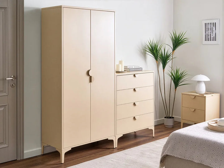 A light beige bedroom furniture set including a tall double-door wardrobe, a four-drawer chest, and a smaller side table, styled in a modern bedroom next to a bed and potted plants.