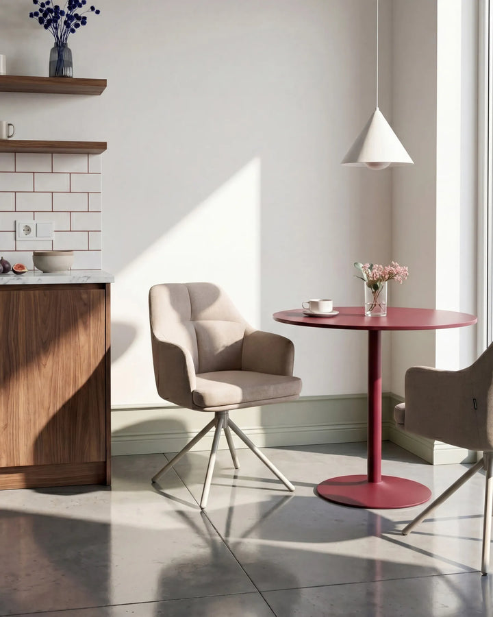 A modern interior scene with a round red table and two upholstered swivel chairs in a bright room with strong sunlight and shadows.