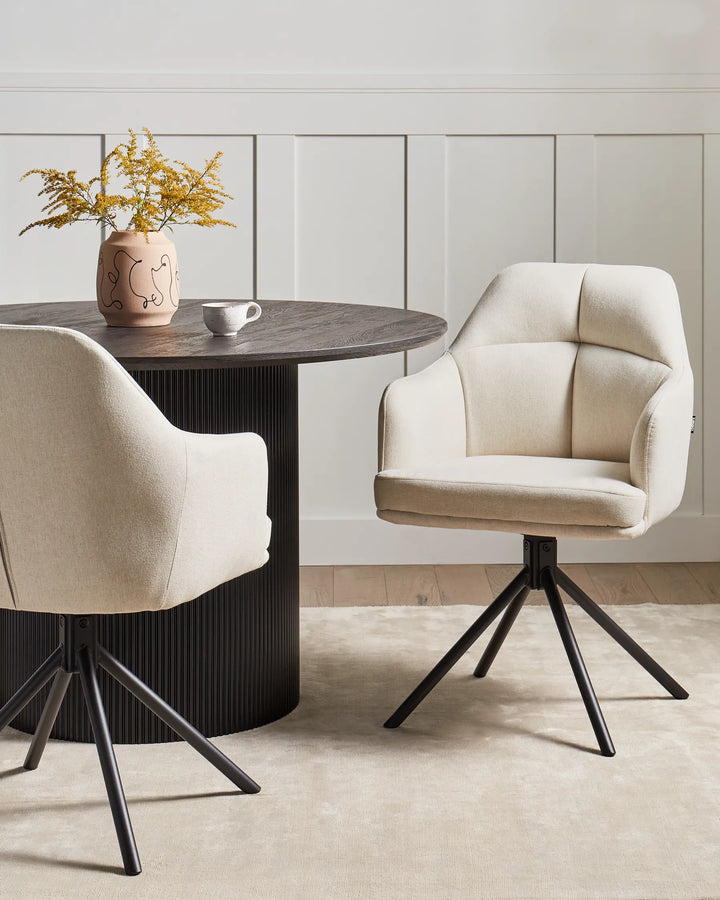 Two beige chairs around a dark wooden table with a vase of flowers on a light wood floor.