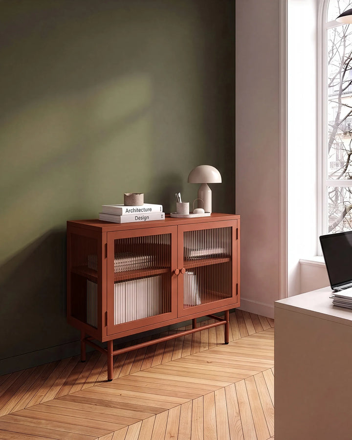 A mid-century modern wooden sideboard cabinet with two glass-paneled doors, styled in a minimalist room with a dark green wall, herringbone wood floor, and a window.