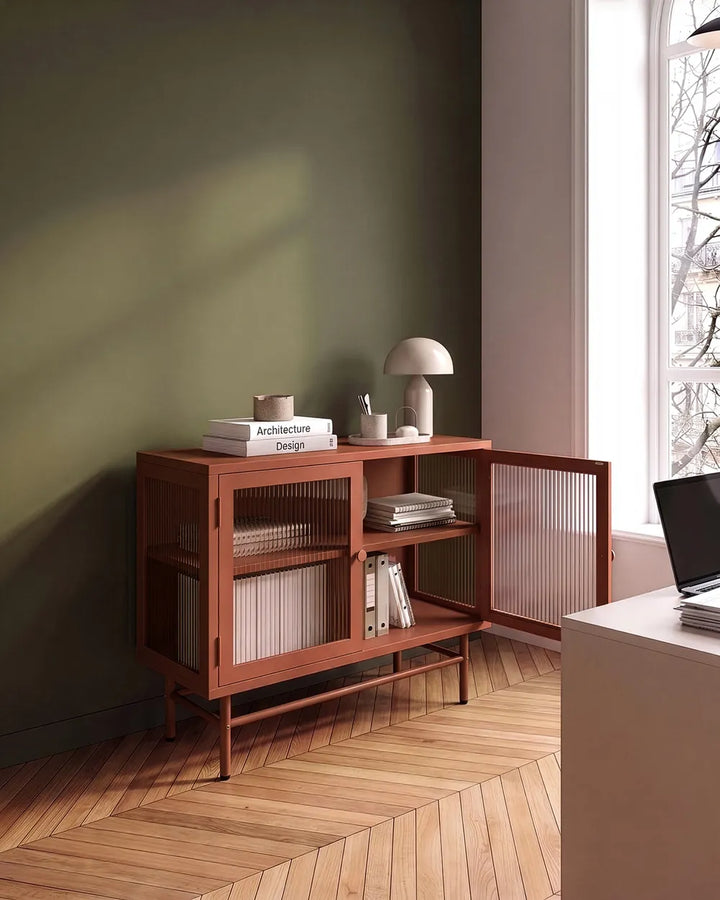 A mid-century modern wooden sideboard cabinet with glass doors and open shelves, styled in a minimalist room with a dark green wall, wood herringbone floor, and a window.
