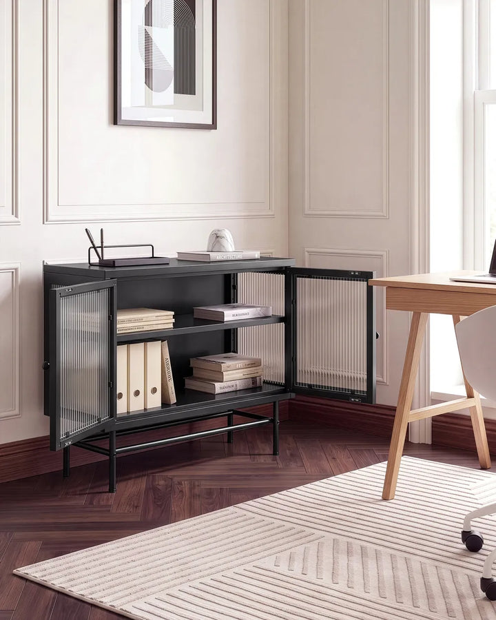 A black metal side cabinet with glass doors and wire shelves, styled in a home office corner next to a wooden desk and chair on a patterned rug.
