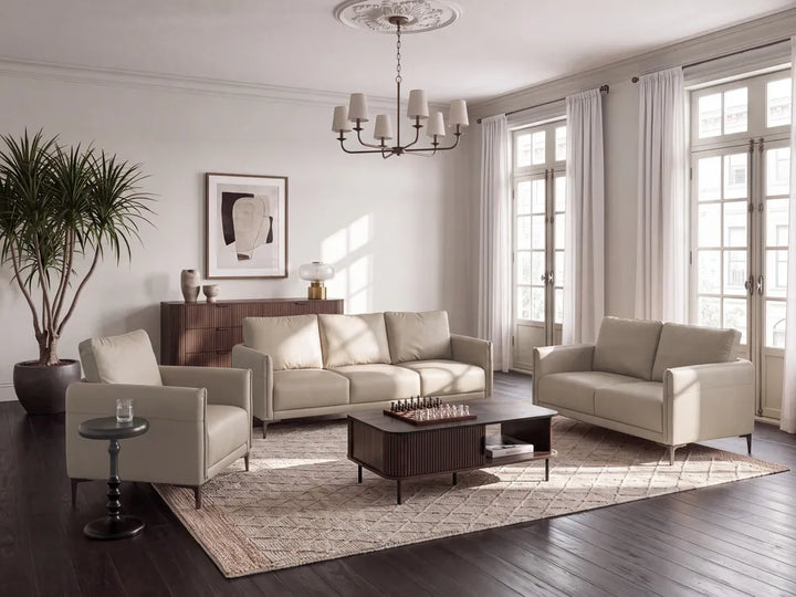 A styled living room featuring a light beige sofa, matching armchair, loveseat, dark wood coffee table, and a patterned area rug on dark hardwood floors.