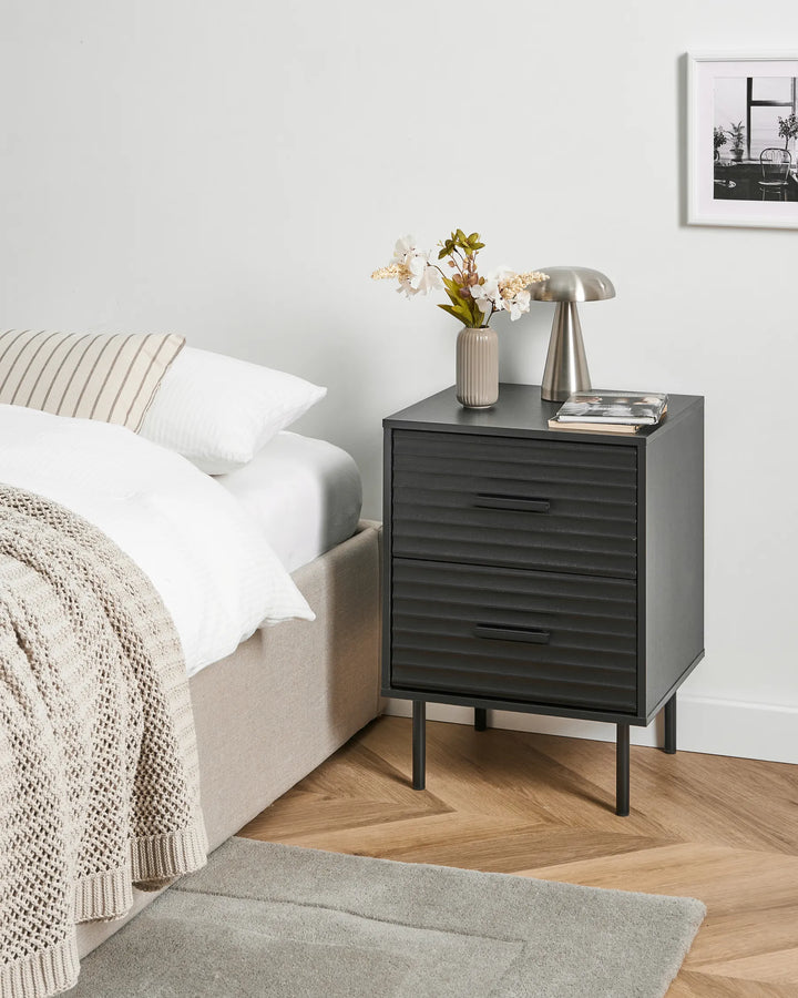 Black nightstand with decorative items next to a bed in a bedroom setting.