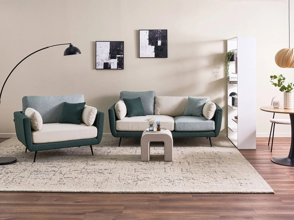 A modern living room setup featuring a teal and cream two-seater sofa and a matching armchair on a large textured cream rug, with a small white coffee table in the center.