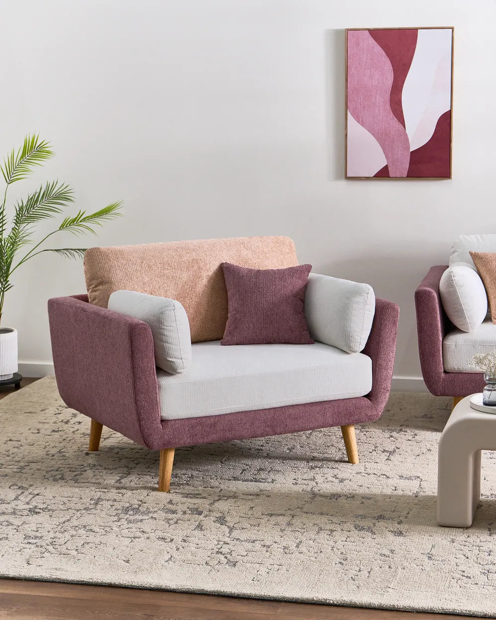 A modern loveseat sofa in dusty rose and white upholstery with light wood legs, styled in a living room setting with a beige rug, a potted plant, and abstract wall art.