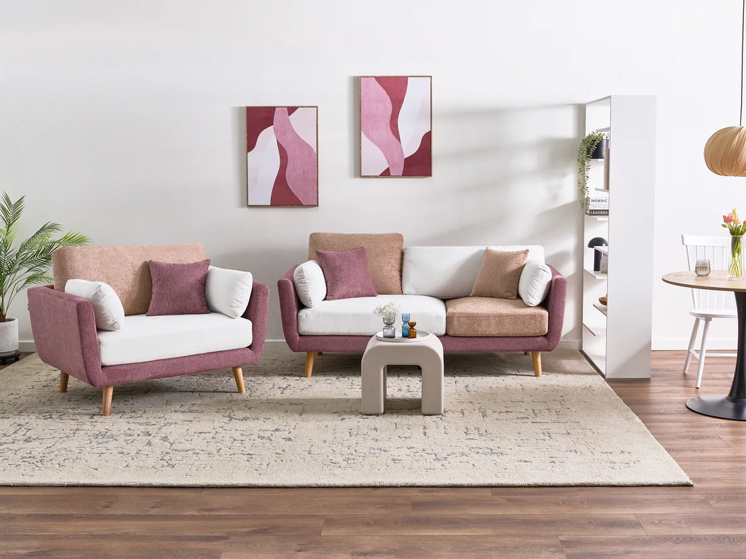 A modern living room setup featuring a mauve-pink and white armchair, a matching three-seater sofa, and a small square side table on a beige rug over dark wood flooring.