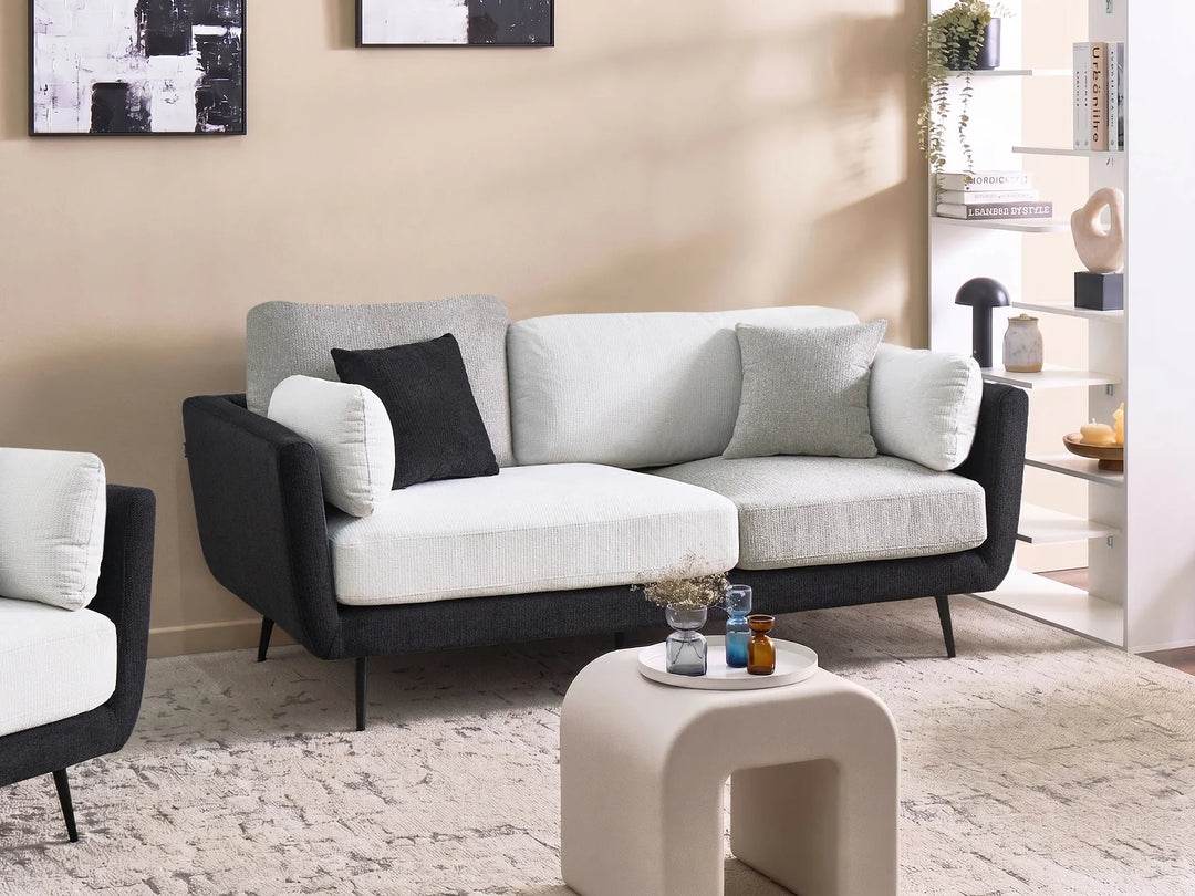 A modern three-seat sofa with a black upholstered frame and light gray and white seat cushions, styled in a contemporary living room setting with a matching armchair, a small white side table, and a textured rug.