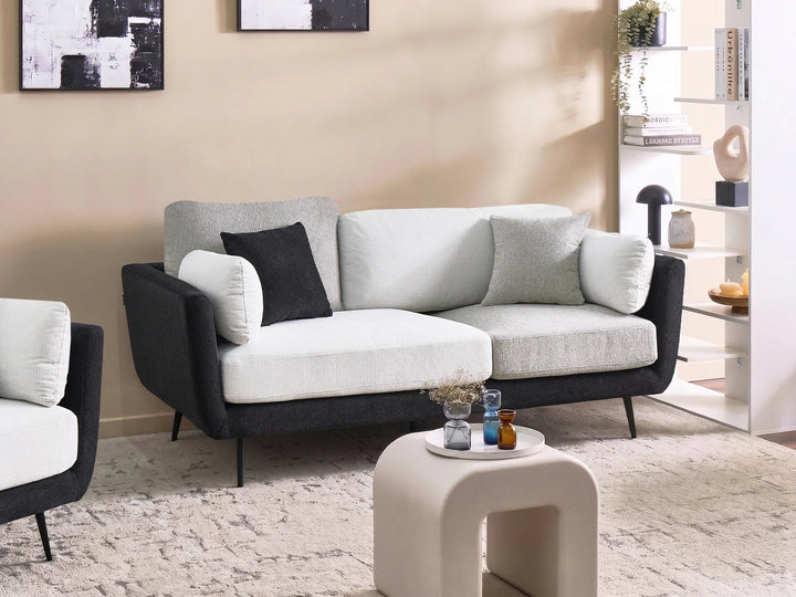 A modern three-seat sofa with a black upholstered frame and light gray and white seat cushions, styled in a contemporary living room setting with a matching armchair, a small white side table, and a textured rug.