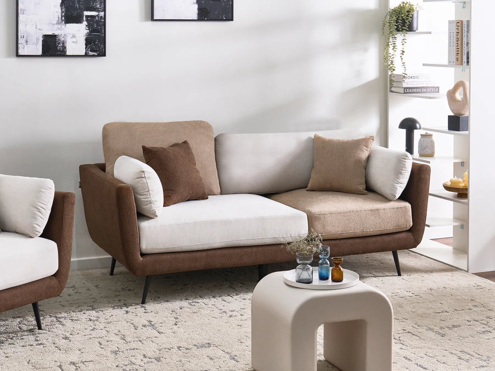 A modern two-seater sofa in brown and beige upholstery with white cushions, styled in a bright, contemporary living room next to a matching armchair.