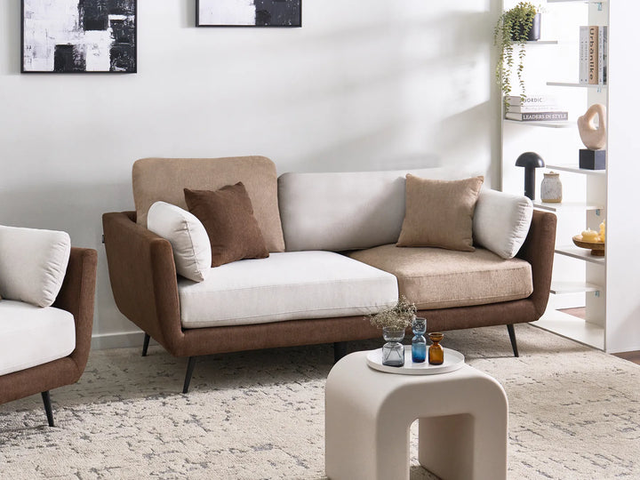 A modern two-seater sofa in brown and beige upholstery with white cushions, styled in a bright, contemporary living room next to a matching armchair.