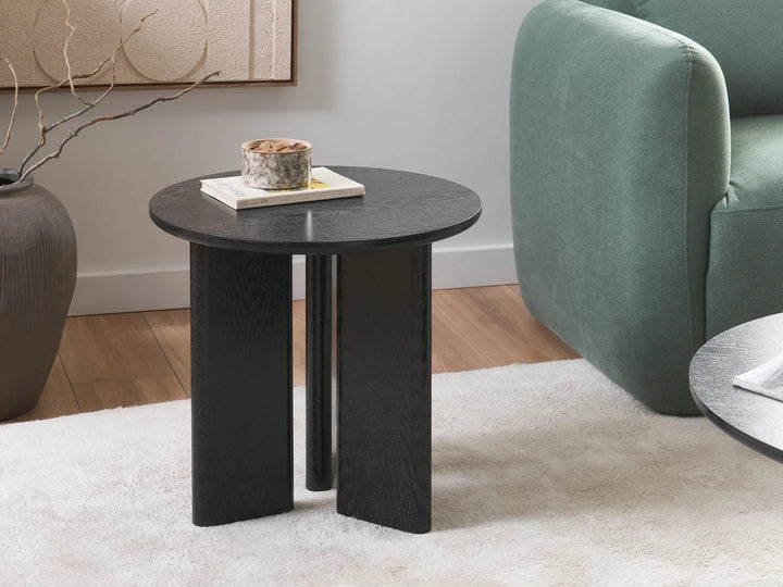 Black side table in a living room setting with a green sofa and decorative items.