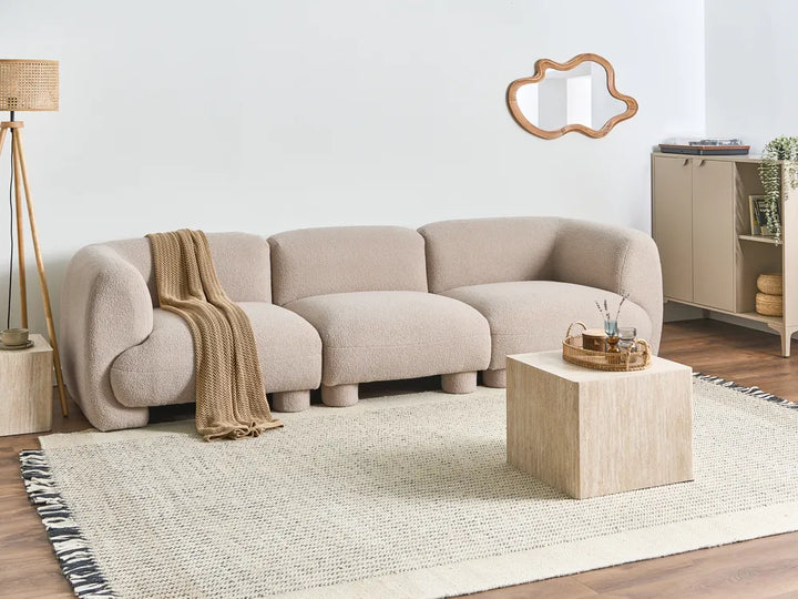 Beige sectional sofa in a modern living room with a wooden coffee table and lamp.