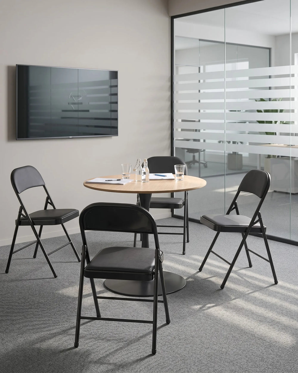 Modern conference room with round table and black chairs, featuring a TV on the wall.