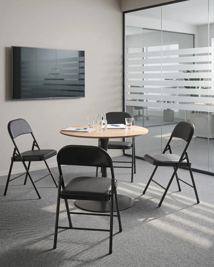 Modern conference room with round table and black chairs, featuring a TV on the wall.