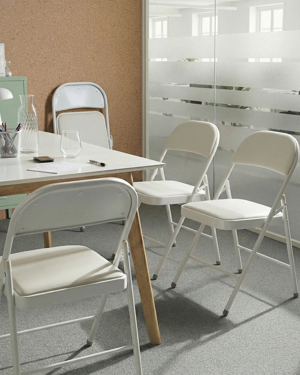 White folding chairs around a table in a room with a glass wall.