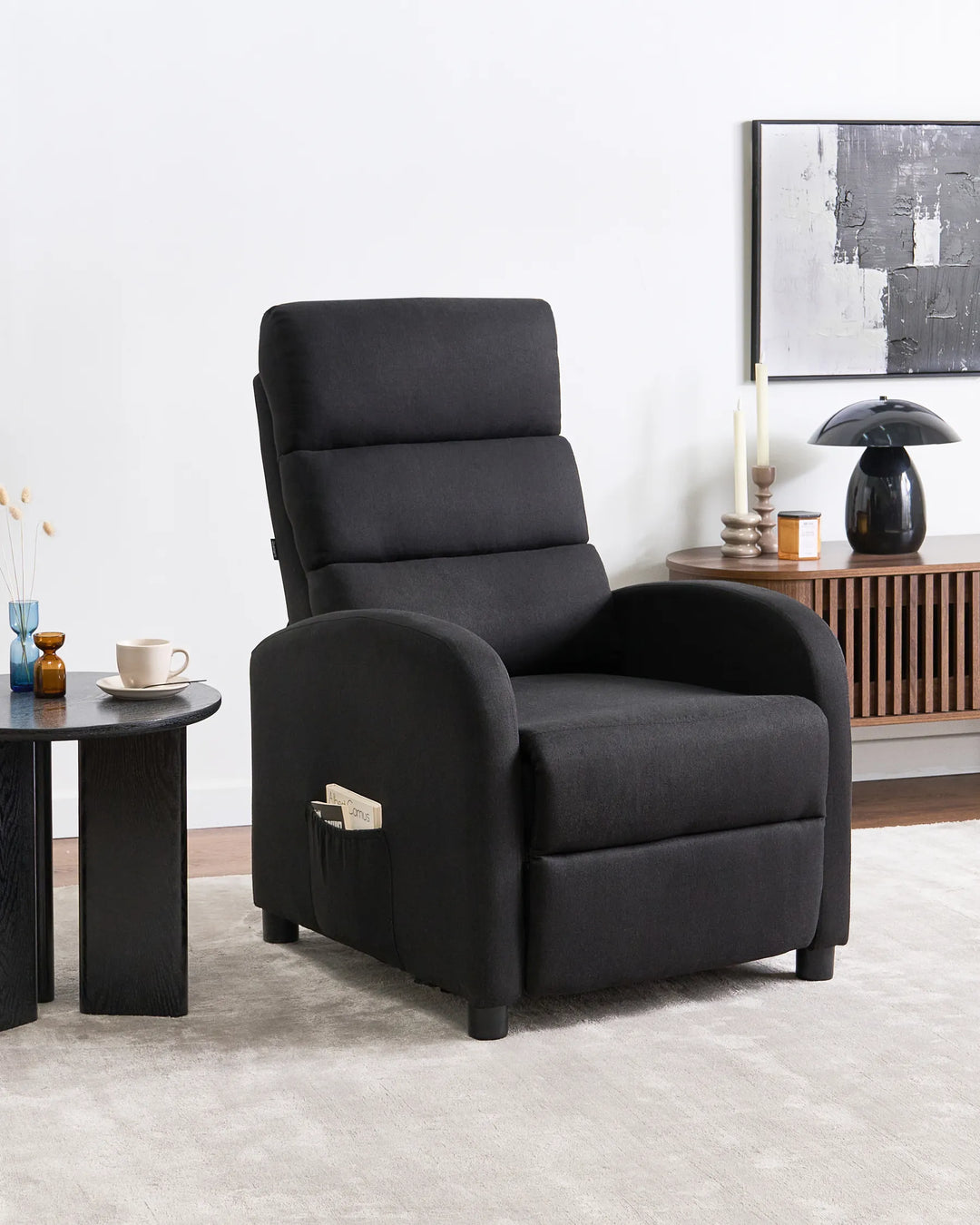 Black recliner chair in a living room setting with a side table and lamp.