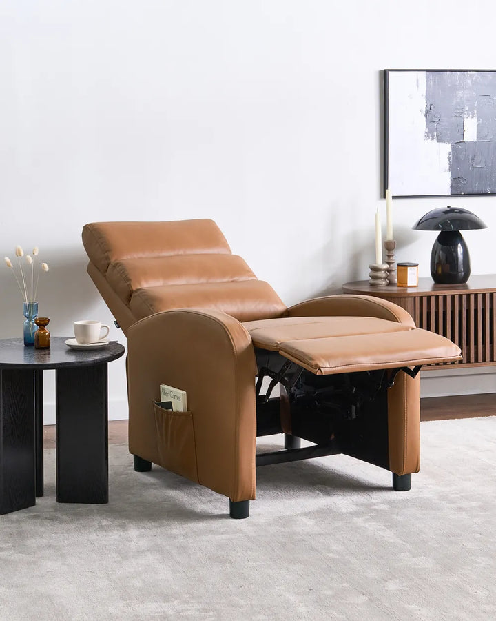 A tan leather recliner chair with the footrest extended, shown in a modern living room setting next to a black side table and console table.