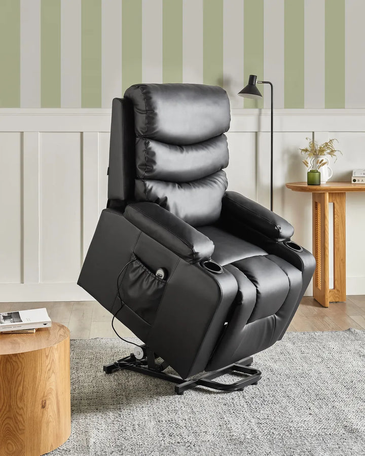 A black leather recliner chair with cup holders and a side pocket, shown in a styled room setting with striped wallpaper, a wooden side table, and a gray rug.