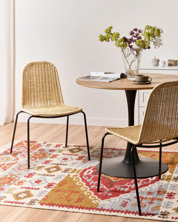 Dining area with wicker chairs, round table, and colorful rug.