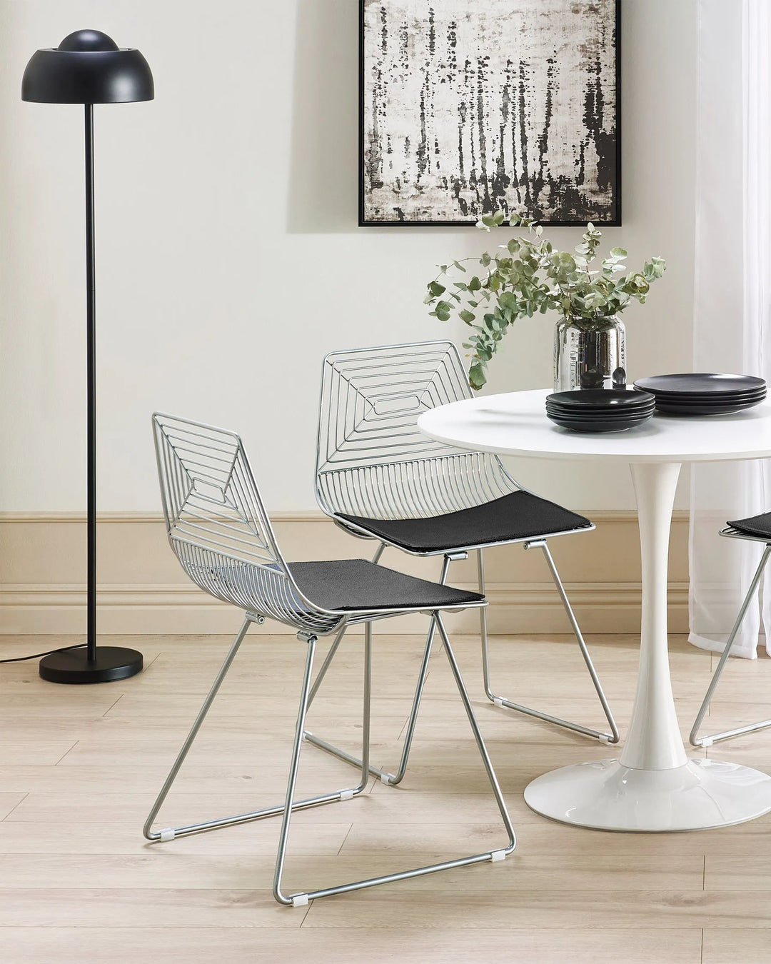 Modern dining area with wire chairs, a white table, and a black floor lamp.