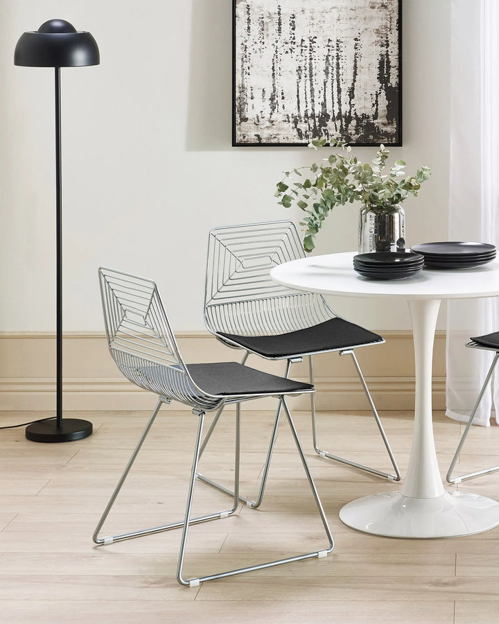 Modern dining area with wire chairs, a white table, and a black floor lamp.