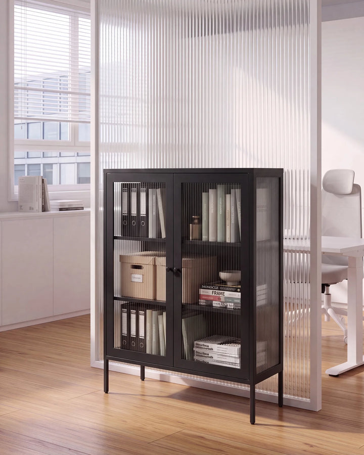 A black metal and glass cabinet with four shelves, styled with books and binders in a modern office setting with a wooden floor and white ribbed glass divider.