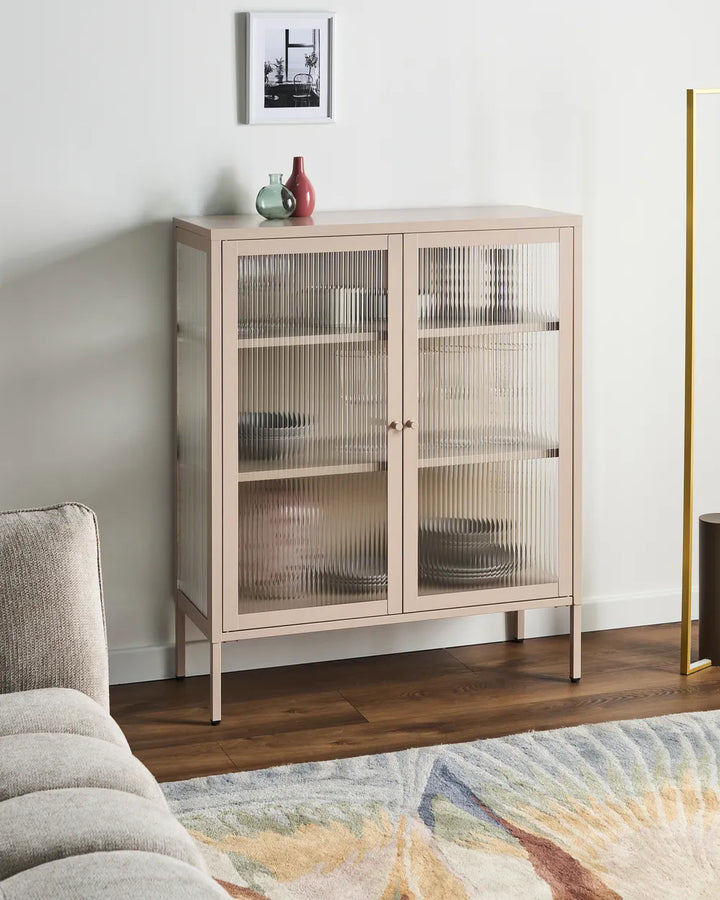 A light beige wooden sideboard cabinet with two ribbed glass doors, styled in a modern living room setting with a wooden floor, a gray sofa, and a patterned rug.