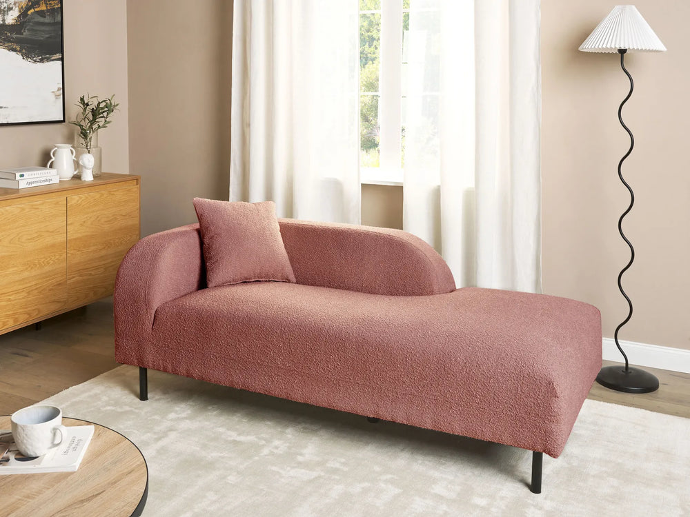 Pink chaise lounge in a living room setting with a wooden sideboard and lamp.