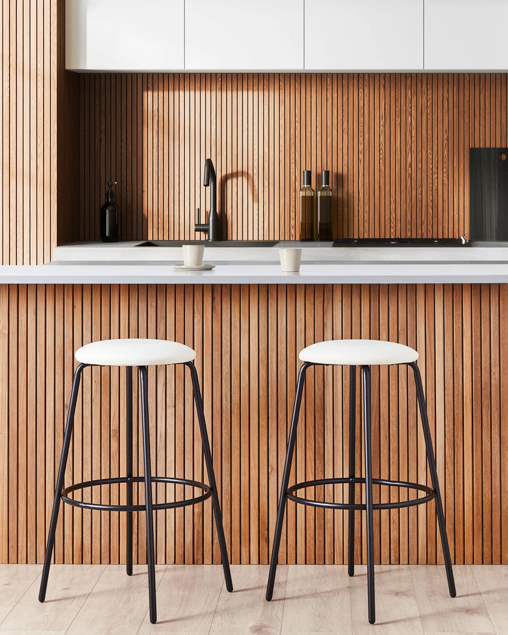 Two bar stools with white seats and black metal legs in a kitchen setting.