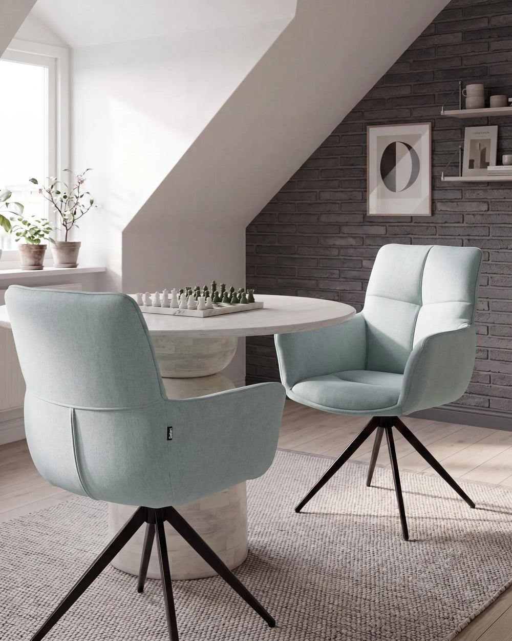 Two modern light blue swivel dining chairs with black metal tripod legs, positioned on a textured rug around a round white table in a stylishly decorated room with a gray brick accent wall.