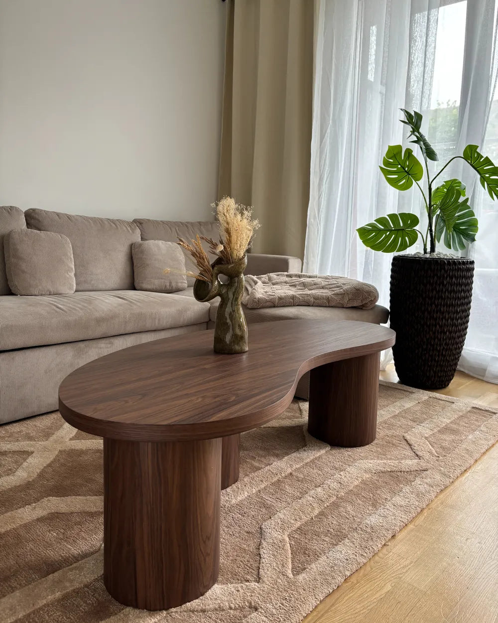 Modern living room with a wooden coffee table, beige sofa, and decorative plant.