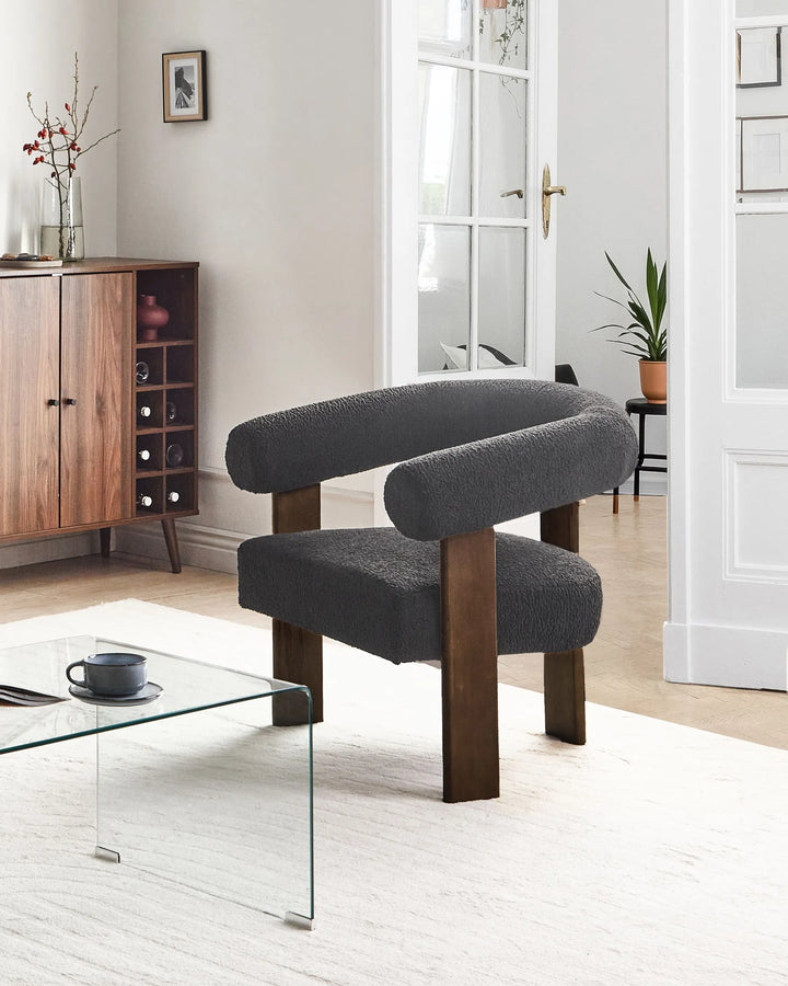 A modern curved armchair with dark gray bouclé upholstery and dark wood legs, shown in a bright, contemporary living room setting.