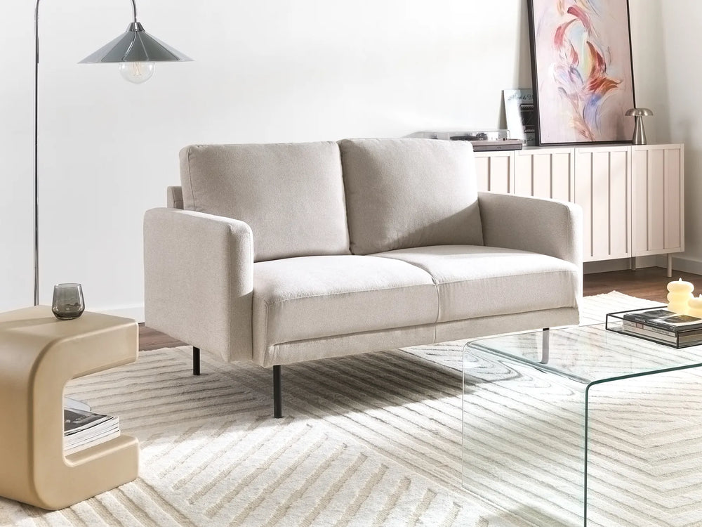 Beige sofa in a modern living room with a glass coffee table and side table.