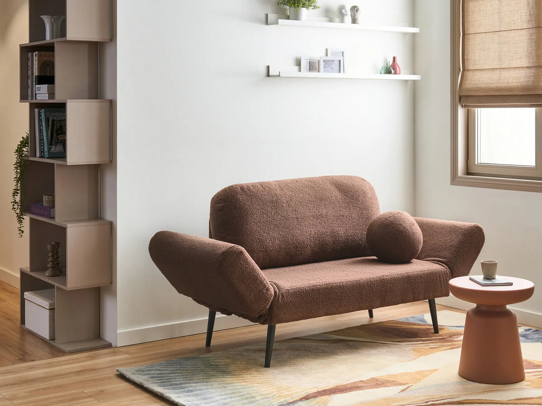 A brown bouclé loveseat sofa with dark metal legs in a modern living room setting, featuring a matching round throw pillow, a terracotta side table, and a light wood floor.
