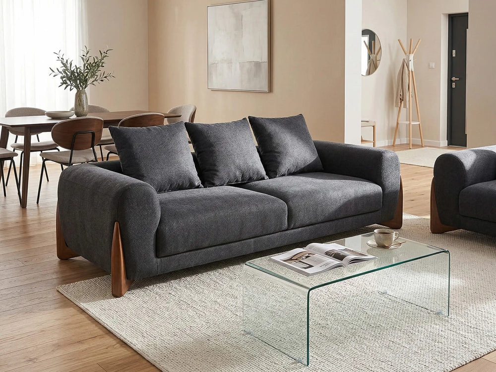 A modern gray fabric loveseat sofa with dark wood legs, styled in a contemporary living room next to a glass coffee table and textured rug.
