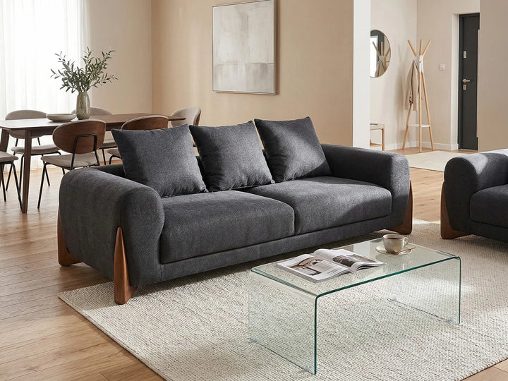 A modern gray fabric loveseat sofa with dark wood legs, styled in a contemporary living room next to a glass coffee table and textured rug.