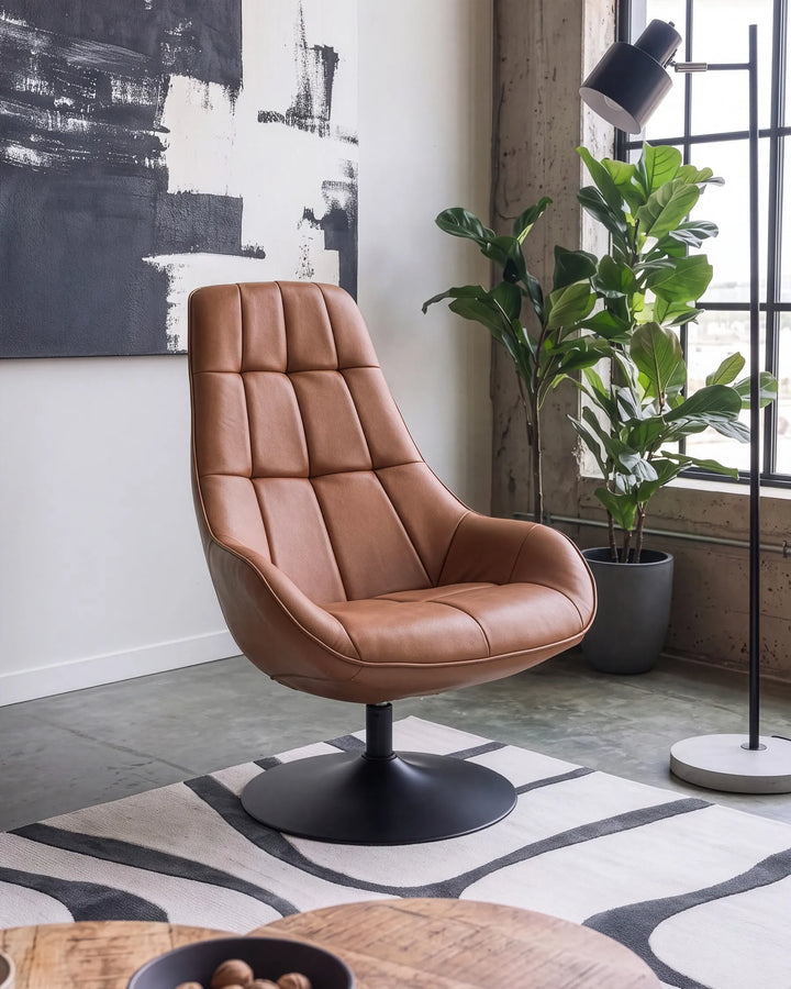 A modern tan leather swivel lounge chair with a high tufted backrest and a black metal pedestal base, styled in a contemporary room with a patterned rug, potted fiddle-leaf fig plant, and abstract wall art.