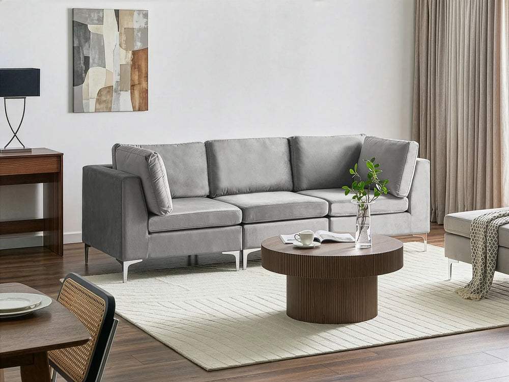 A modern light gray fabric sectional sofa in a styled living room setting with a round wooden coffee table, cream rug, and wall art.
