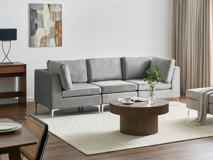 A modern light gray fabric sectional sofa in a styled living room setting with a round wooden coffee table, cream rug, and wall art.