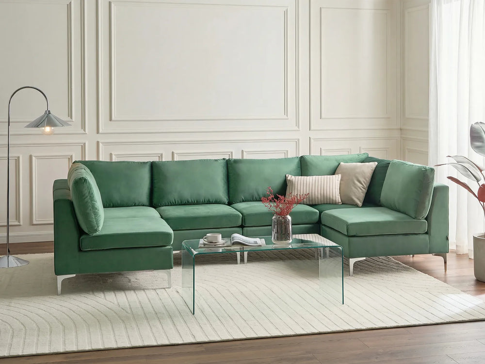 A green sectional sofa with a chaise lounge in a modern living room setting, styled with neutral throw pillows, a glass coffee table, and a textured rug.