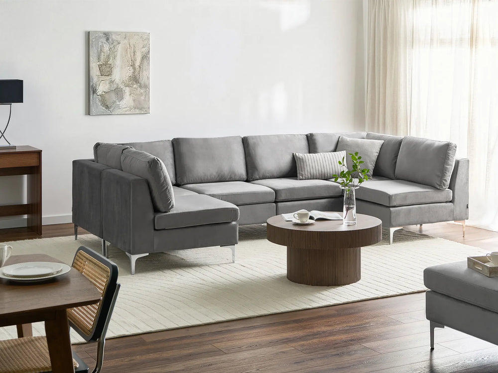 A modern gray fabric sectional sofa with a left-facing chaise lounge, styled in a bright, contemporary living room with a round wooden coffee table and a cream rug.