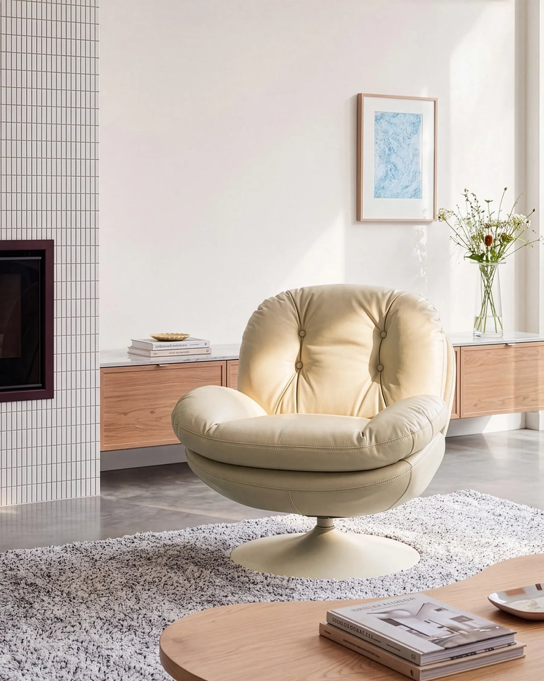 A cream-colored tufted leather swivel lounge chair in a modern, sunlit living room setting.