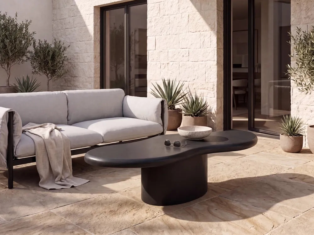 Modern outdoor patio furniture set featuring a light gray three-seater sofa and a dark charcoal wavy oval coffee table on a stone tiled patio.