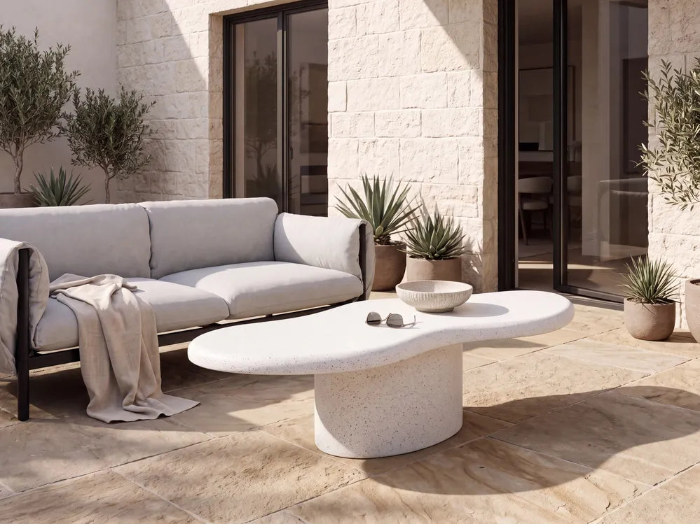 Modern outdoor patio furniture set featuring a light gray fabric sofa and a matching organic-shaped stone coffee table on a stone-tiled patio.