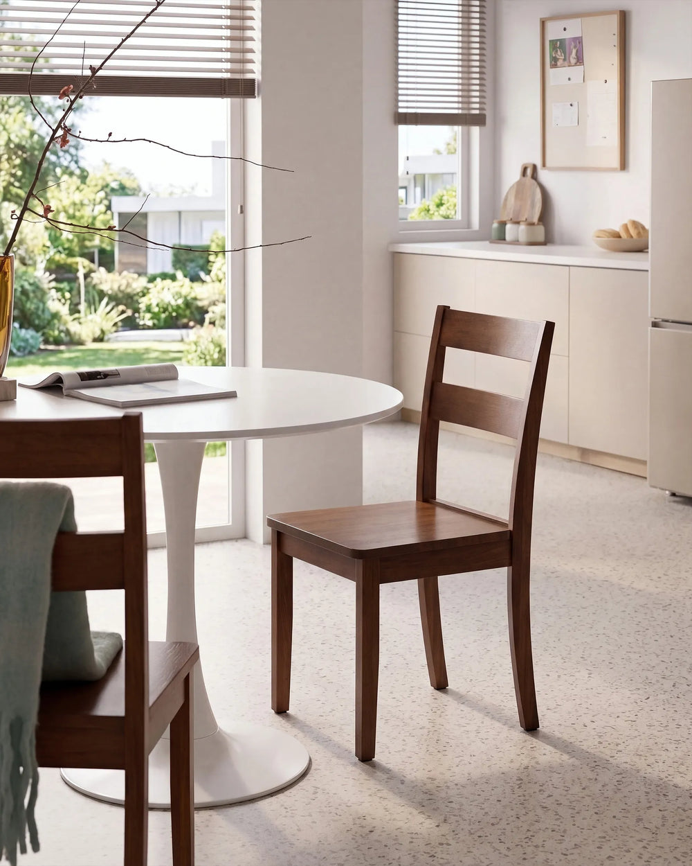 A modern wooden dining chair with a slatted back and seat, shown in a bright, contemporary kitchen or dining area next to a white round table.
