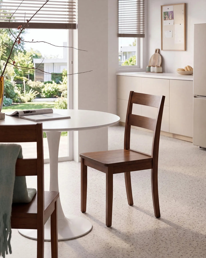 A modern wooden dining chair with a slatted back and seat, shown in a bright, contemporary kitchen or dining area next to a white round table.