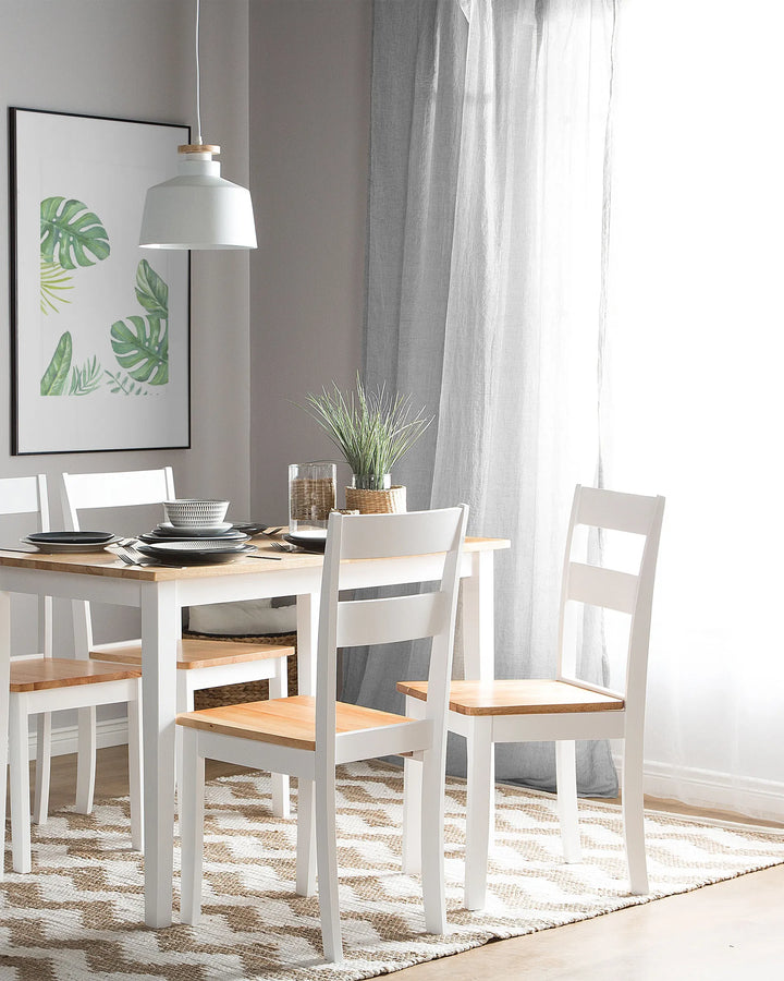 Dining room with wooden table and white chairs, featuring a plant and framed artwork on the wall.