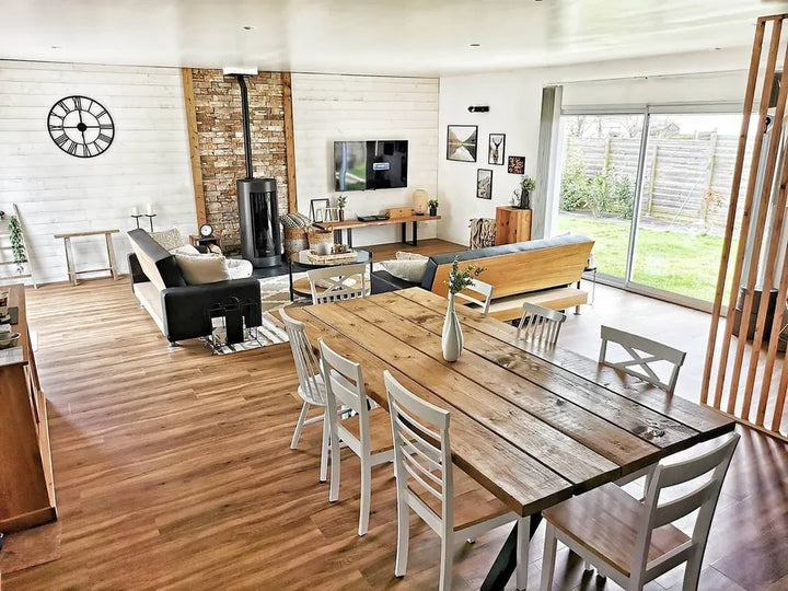 Modern living room with wooden dining table and chairs, TV, and large windows.