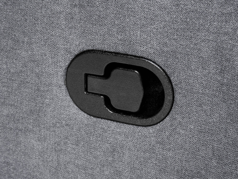 A close-up of a black oval-shaped plastic component with a keyhole-shaped cutout, mounted on a textured gray fabric surface.